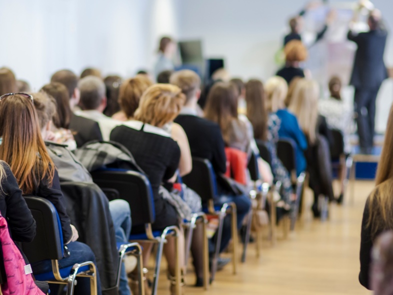 En grupp människor sitter på stolar i ett konferensrum och lyssnar på en presentation.