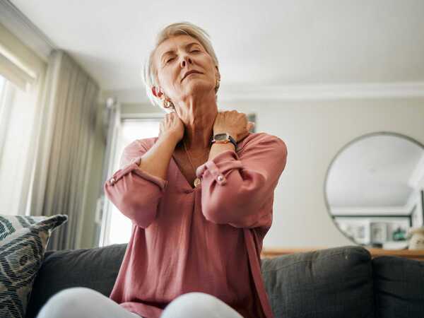 En person sitter i en grå soffa och stretchar sin nacke med händerna.