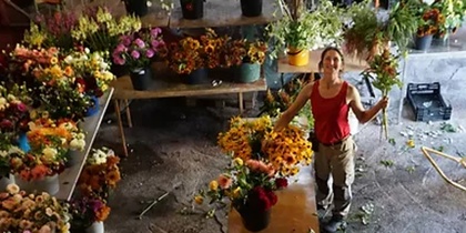 En person står i en blomsterverkstad omgiven av bord fyllda med färgglada blommor och växter.