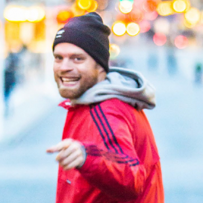 Person i röd jacka och svart mössa står på en stadsgata med suddig bakgrund och ljusprickar.