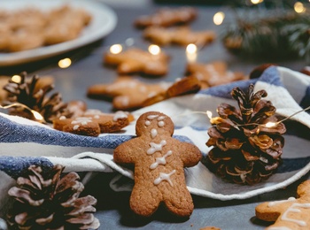 Pepparkakor dekorerade med glasyr ligger på ett bord med kottar, granris, tygservett och julbelysning.