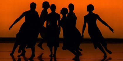 Sex dansare i silhuett poserar mot en orange bakgrund på en scen.