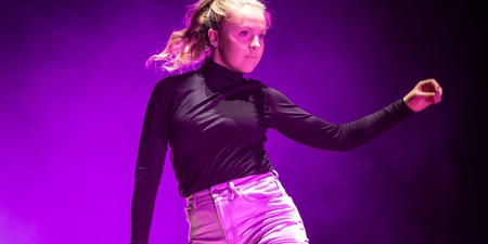 En person dansar barfota på en scen med lila ljus och rökeffekter.