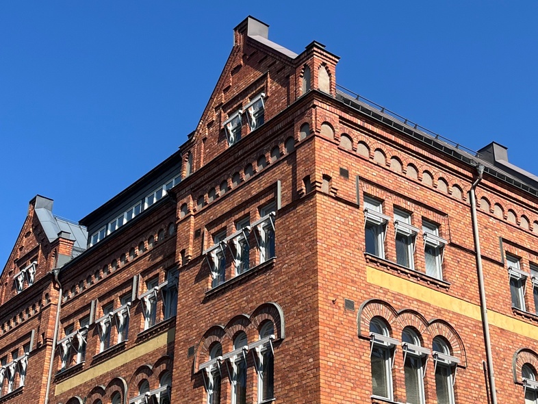 Tegelfasad på en äldre byggnad med många fönster mot en klarblå himmel.