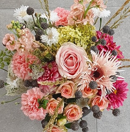 En bukett med blandade blommor i rosa, vitt och grönt mot en grå bakgrund.