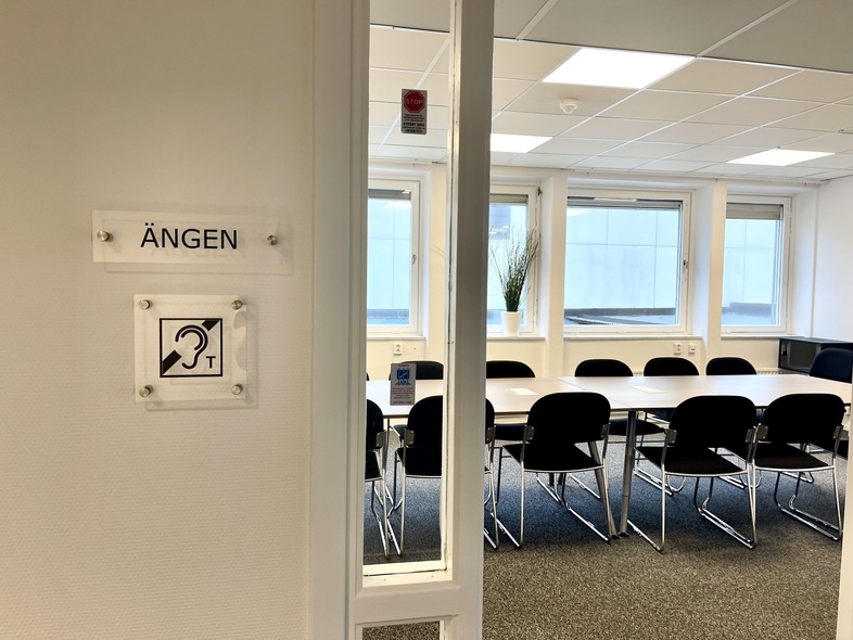 Ingång till ett konferensrum med skylten 'Ängen' och symbol för hörslinga på väggen.