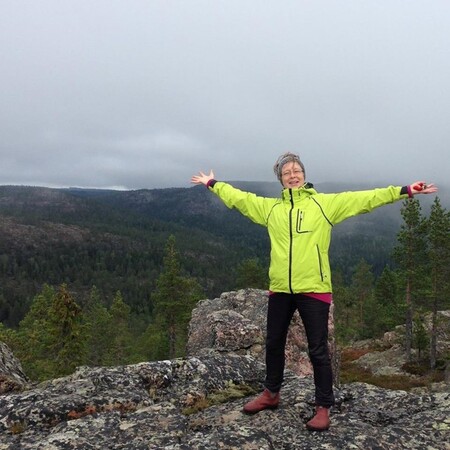 Kvinna i guljacka står vid en brant och håller ut armarna.