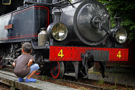 Ett barn sitter på huk framför ett gammalt svart ånglok med röd front och siffran 4.