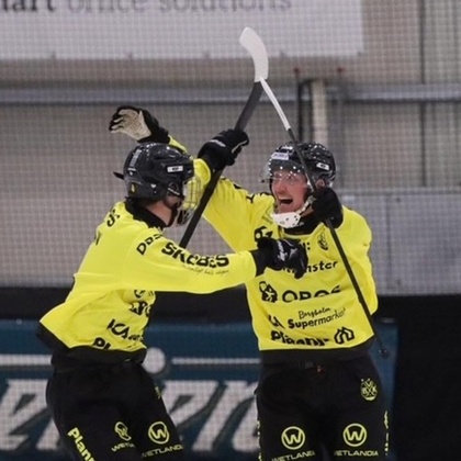 Två bandyspelare i gula tröjor firar på isen under en match.