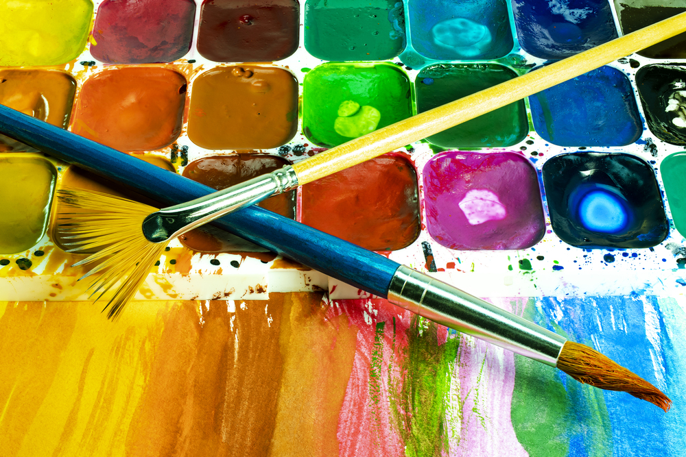 Närbild av en färgglad akvarellpalett med två penslar och målade färgfält.