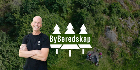 Man ler framför en skogsbakgrund med texten 'ByBeredskap' och tre vita granar.