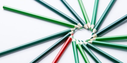 Flera gröna och en röd färgpenna ligger i en cirkel på ett vitt underlag.