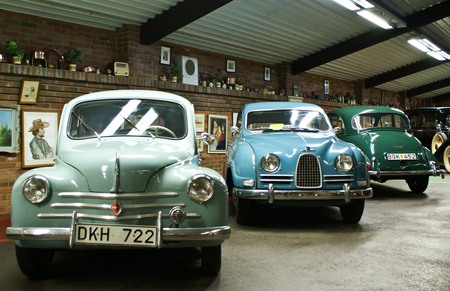 Tre klassiska bilar står parkerade inomhus i ett museum med tavlor och prydnader på väggen bakom.