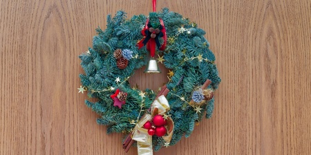 En julkrans med röda dekorationer, kottar och en guldfärgad rosett hänger på en trädörr.