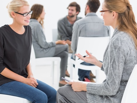 Två kvinnor sitter mittemot varandra och samtalar i en ljus lokal, andra personer syns i bakgrunden.