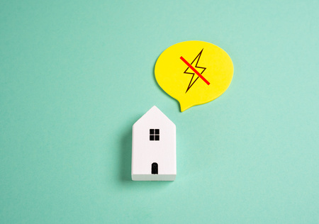 En vit modell av ett hus med en pratbubbla som visar en överkryssad blixt, på grön bakgrund.