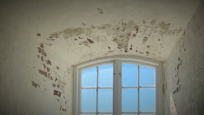 Ett gammalt fönster med välvt tak och avflagad puts på väggarna, ljusblå himmel utanför.