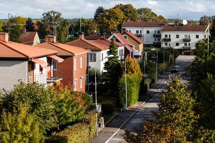 En lugn bostadsgata med radhus och gröna träd i ett villaområde under hösten.