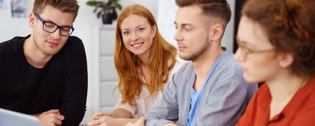 Fyra unga vuxna sitter vid ett bord och arbetar tillsammans med en laptop och anteckningar.