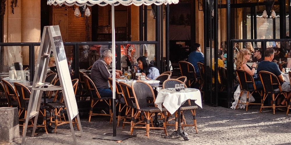 Uteservering på ett parisiskt café med människor som sitter vid bord under en grön markis.