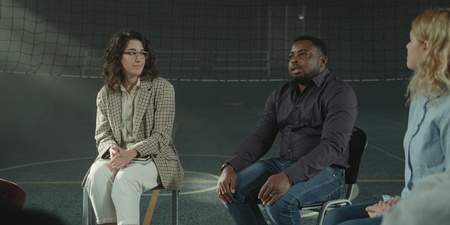 Fyra personer sitter i en cirkel och samtalar i en sporthall med nät i bakgrunden.