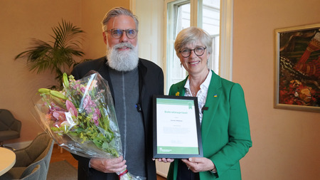 Christer Mattsson med blommor och Ulrika Heie med diplom står bredvid varandra och ler mot kameran.