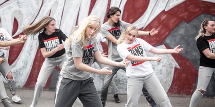 En grupp unga personer dansar hiphop utomhus framför en graffitivägg.