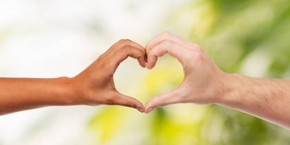 Två händer i olika hudtoner formar ett hjärta mot en suddig grön bakgrund.