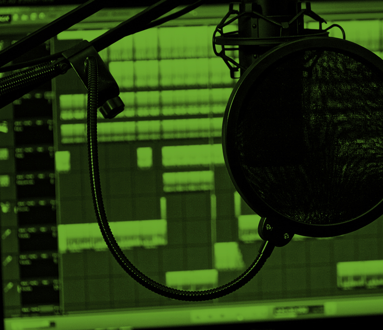 En mikrofon med popfilter framför en datorskärm som visar ljudredigeringsprogram, i grönt ljus.