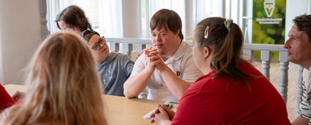 En grupp personer sitter runt ett bord och samtalar i ett ljust rum.