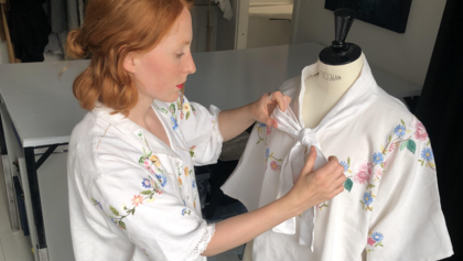 Kvinna knyter en rosett på en vit broderad blus som sitter på en provdocka.