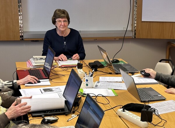 Fyra personer sitter runt ett bord med bärbara datorer, papper och pennor i ett mötesrum.