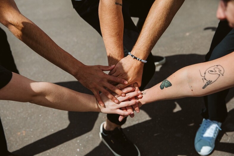 Fem personer räcker fram sina händer och lägger dem ovanpå varandra.