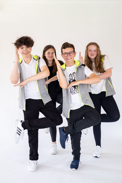 Fyra ungdomar poserar tillsammans i dansställning mot vit bakgrund, alla ler och bär liknande kläder.
