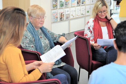 Fyra personer sitter i en cirkel och läser papper i ett ljust rum, troligen under ett möte eller en studiecirkel.