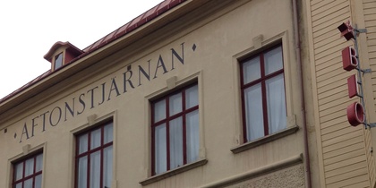 Fasad av en äldre byggnad med skylten 'AFTONSTJÄRNAN' och röda fönster, på en sluttande gata.