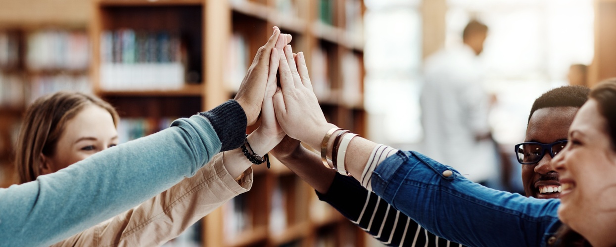 Fyra unga personer gör en high five tillsammans i ett bibliotek.