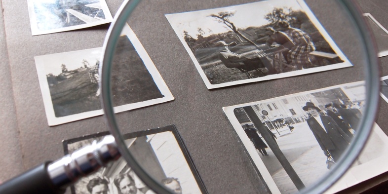 Ett fotoalbum med svartvita fotografier granskas med ett förstoringsglas.