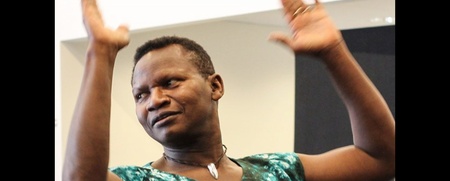 En person med kort hår och grön mönstrad tröja dansar med armarna upplyfta.