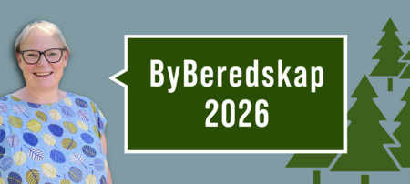 Person i blå tröja med lövmönster står bredvid en skylt med texten 'ByBeredskap 2026' mot grön bakgrund och granar.