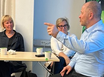 Fyra personer från Demokratiskolan sitter runt ett bord i ett mötesrum på SV Bollnäs och samtalar, en man gestikulerar medan han pratar.