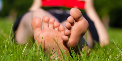 En person ligger på gräset och läser en röd bok, bara fötterna syns tydligt i förgrunden.