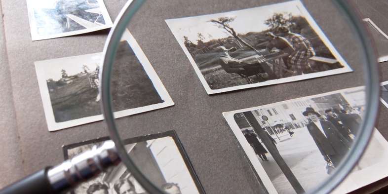 Ett fotoalbum med svartvita fotografier granskas med ett förstoringsglas.