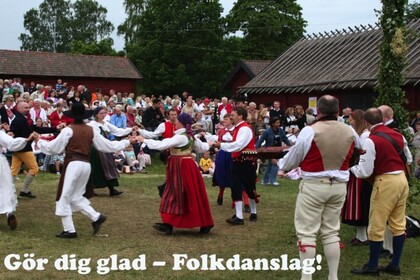 Människor i traditionella folkdräkter dansar i ring utomhus inför en publik.