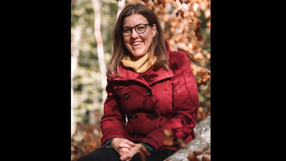 Person med röd kappa och gul halsduk sitter utomhus bland höstlöv.