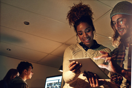 Två personer samarbetar vid en surfplatta i ett kontorsutrymme med dämpad belysning.