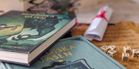 Två böcker om nordiska väsen, tärningar och en hoprullad pappersrulle på ett bord.