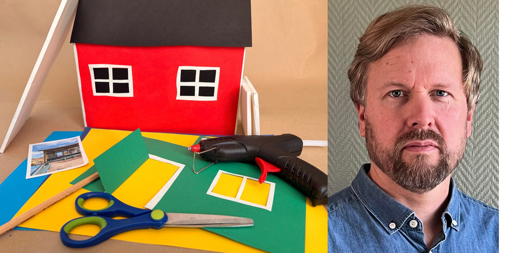 En man med skägg och blå skjorta bredvid ett pysselbord med färgat papper, sax, lim och en modell av ett rött hus.