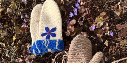 Fyra par stickade vantar i olika färger och mönster ligger på marken bland torra blad och små lila blommor.