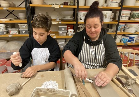 En pojke och en kvinna arbetar med lera vid ett bord i en keramikverkstad.